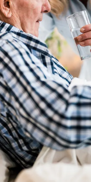 An elderly man receives a glass of water.